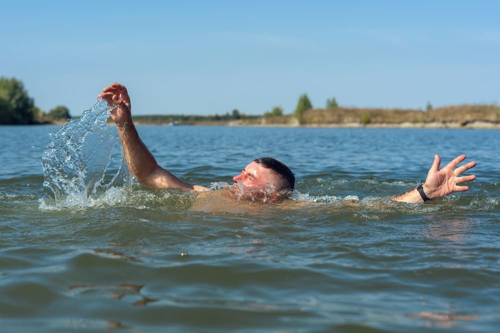 Man struggling to swim in open water, splashing with raised arms and a distressed expression.