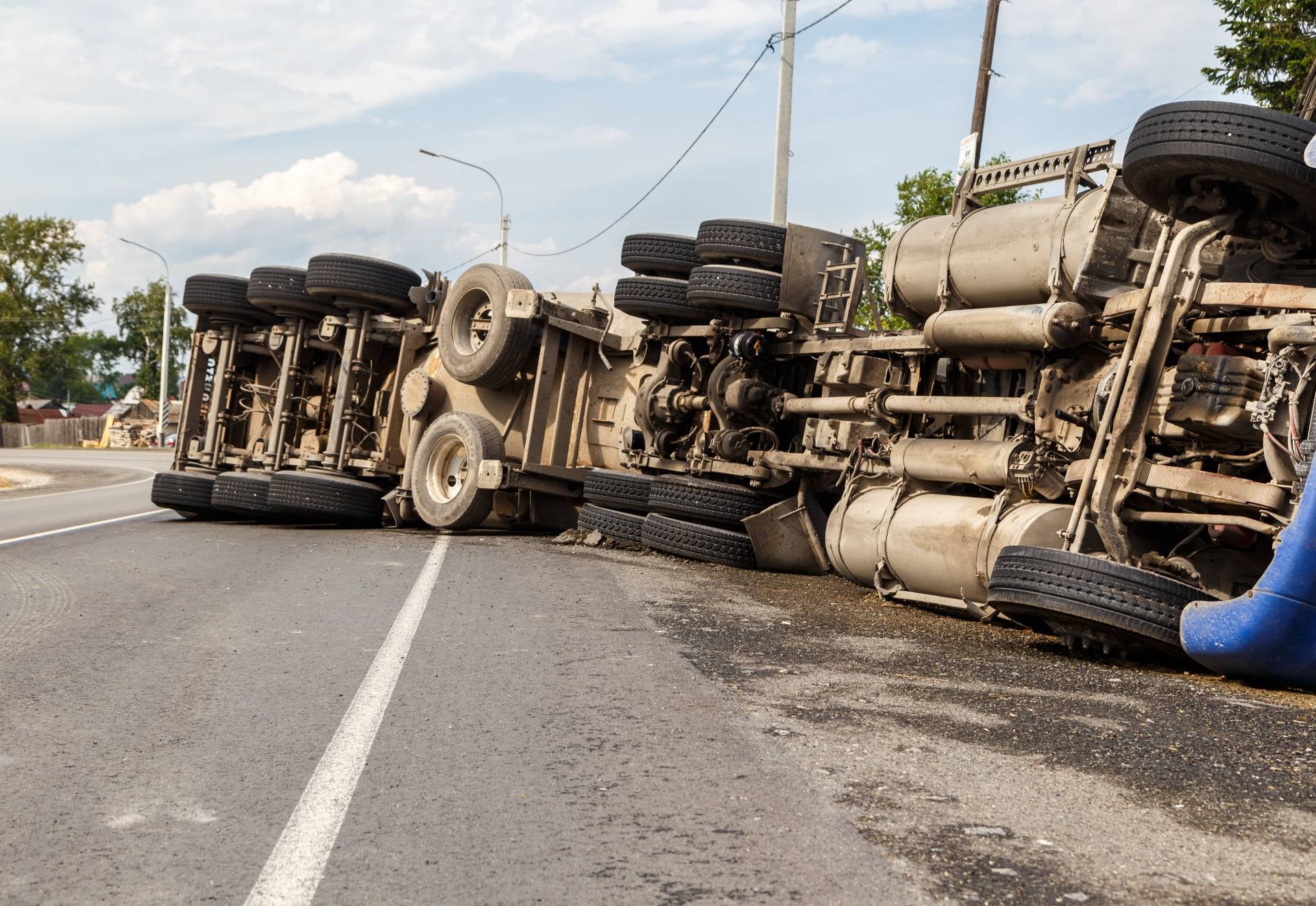 Overturned semi-trailer truck lying on its side across an asphalt road with spilled contents visible.