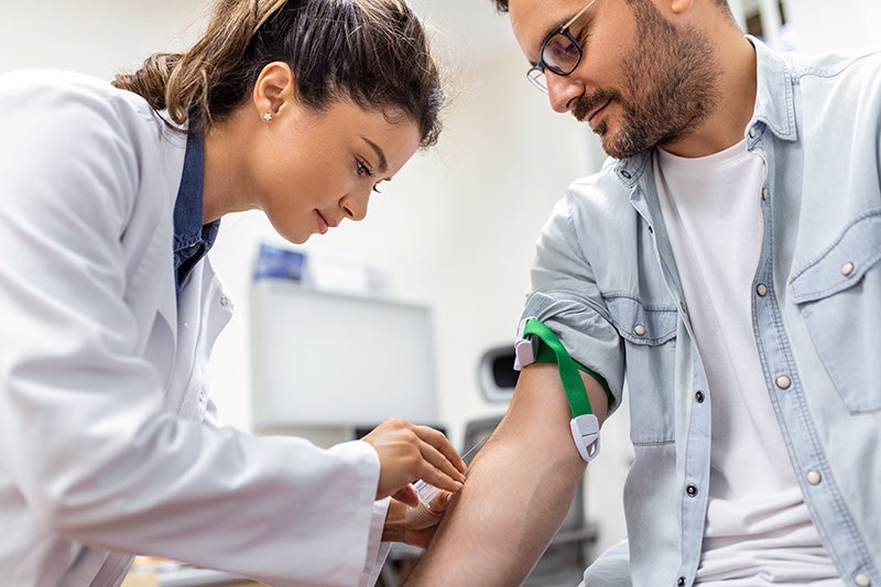 A healthcare worker draws blood from a patient's arm in a clinical setting.