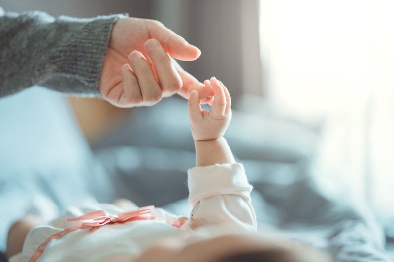 A newborn baby's hand reaching up to grasp an adult's finger in a tender moment.