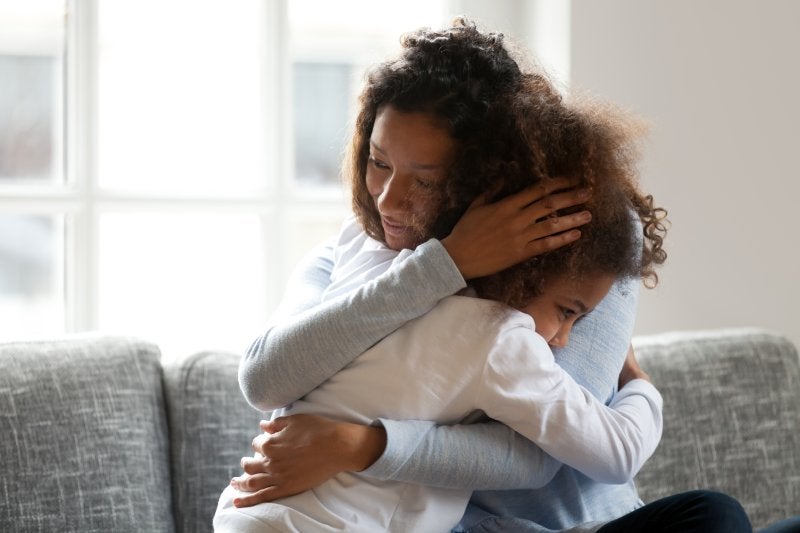 A loving mother hugging her young daughter comforting her on a couch.