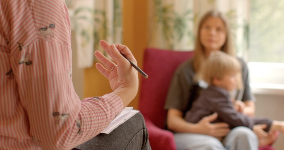 A person in a striped shirt holding a pencil across from a blurry mother holding a child.