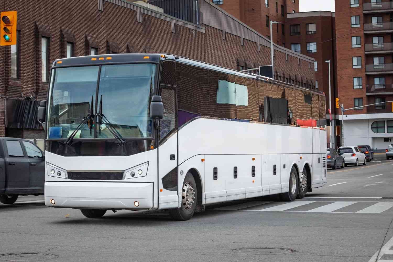 A large white passenger bus with black trim driving on a city street past red brick buildings.