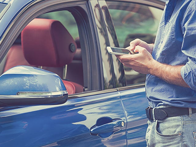 Person standing by a blue car and using a smartphone