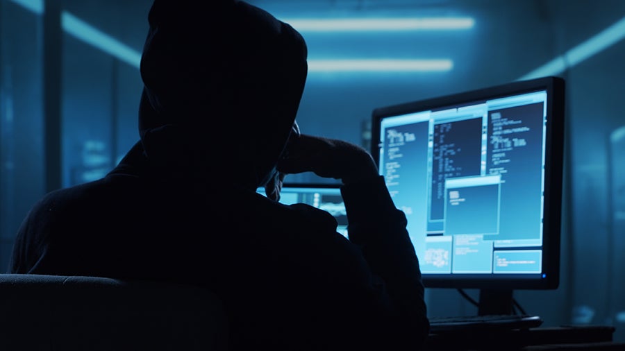A person in a hooded sweatshirt sits facing a computer screen displaying lines of code.