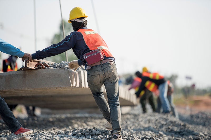 Construction workers, seen from behind, installing railroad tracks and ties on a bed of gravel.