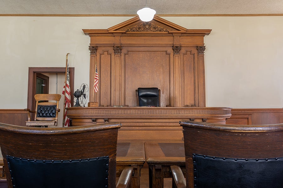 A wooden judge's bench sits in a courtroom, with rows of empty chairs facing it.