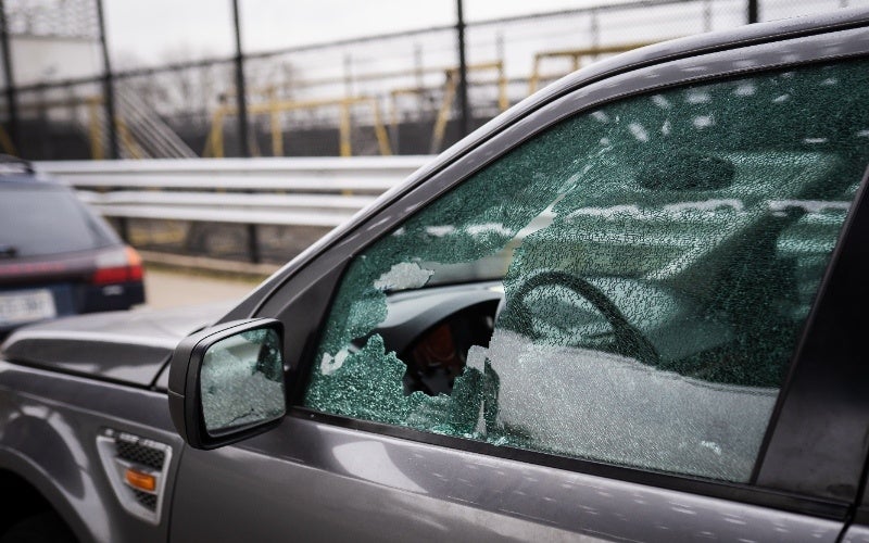 The front driver's-side window of a gray SUV is shattered with a large hole in the lower corner.
