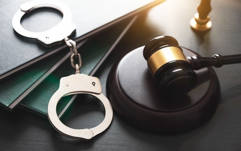Silver handcuffs resting on green books, next to a black and gold judge's gavel and sound block.