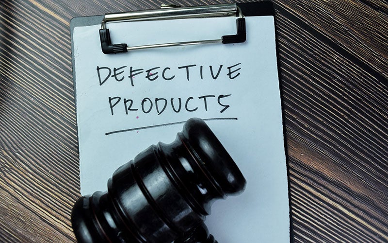 A clipboard with 'DEFECTIVE PRODUCTS' written on paper and a judge's gavel resting partly on it.