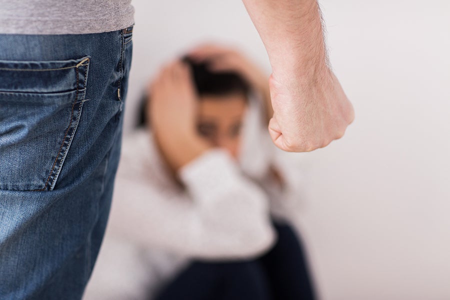A man's clenched fist in the foreground, with a blurring woman crouching fearfully in the background.