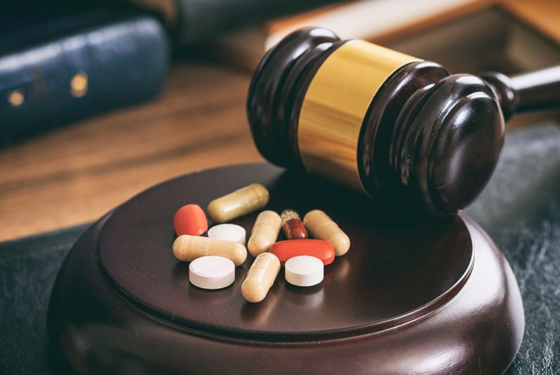A gavel resting on its block, with various pills and capsules scattered across the block.