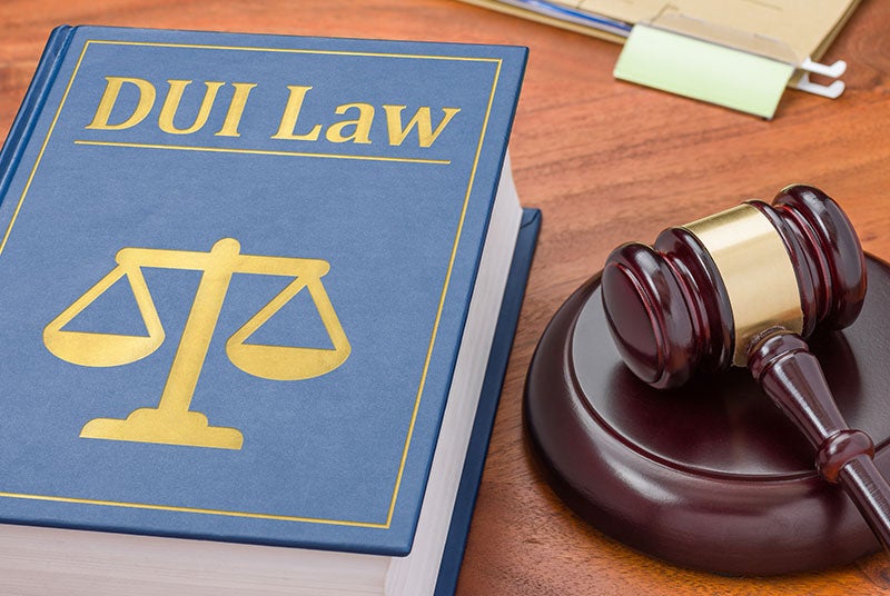 A blue book titled 'DUI Law' with a golden scales of justice emblem, next to a wooden gavel.