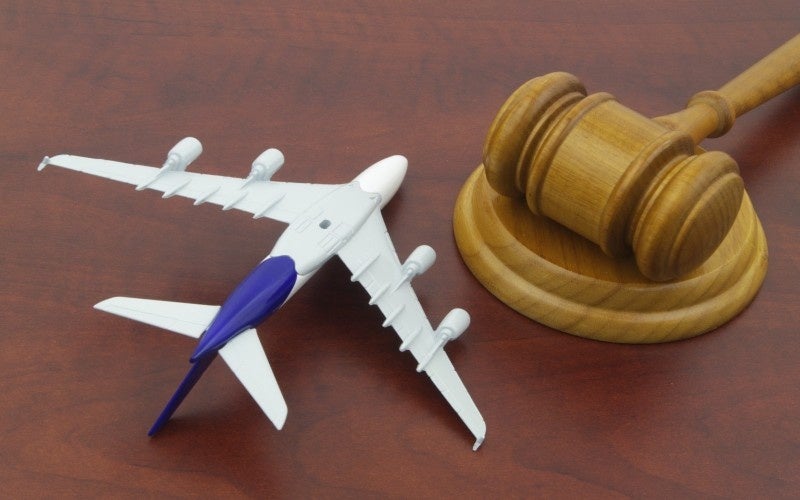 A wooden gavel resting on a block to the right of a model airplane on a dark wooden surface.