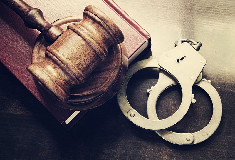 A wooden gavel and handcuffs rest on top of a thick legal book, symbolizing justice and legal proceedings.