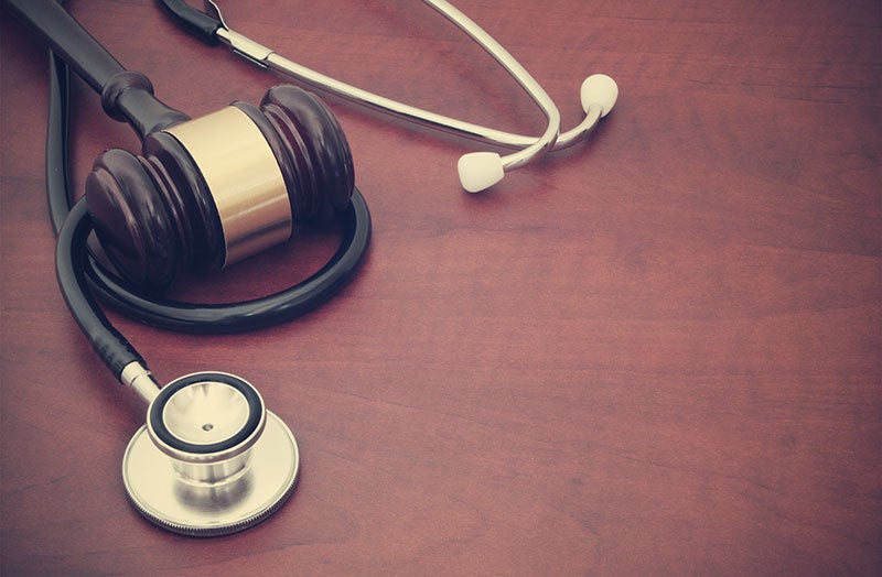 A judge's gavel rests on a stethoscope on a wooden table, representing healthcare law.