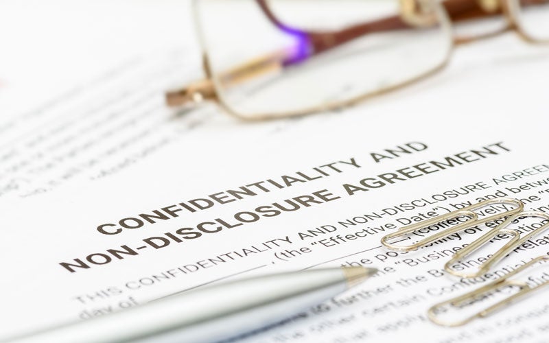 A close-up of a confidentiality and non-disclosure agreement document with a pen, eyeglasses, and paper clips.