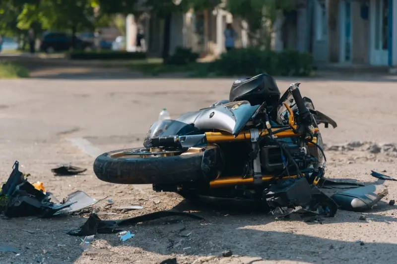 A damaged motorcycle lies on the pavement surrounded by debris and scattered plastic.