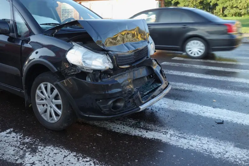 Front view of a black car with severe damage to its hood, grille, and bumper after a collision.