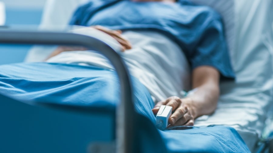 Patient in a hospital bed, wearing a blue gown, with an IV line and a pulse oximeter on their finger.