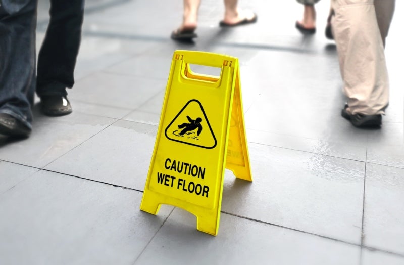 A bright yellow 'CAUTION WET FLOOR' sign on a tiled floor with blurred people walking by.