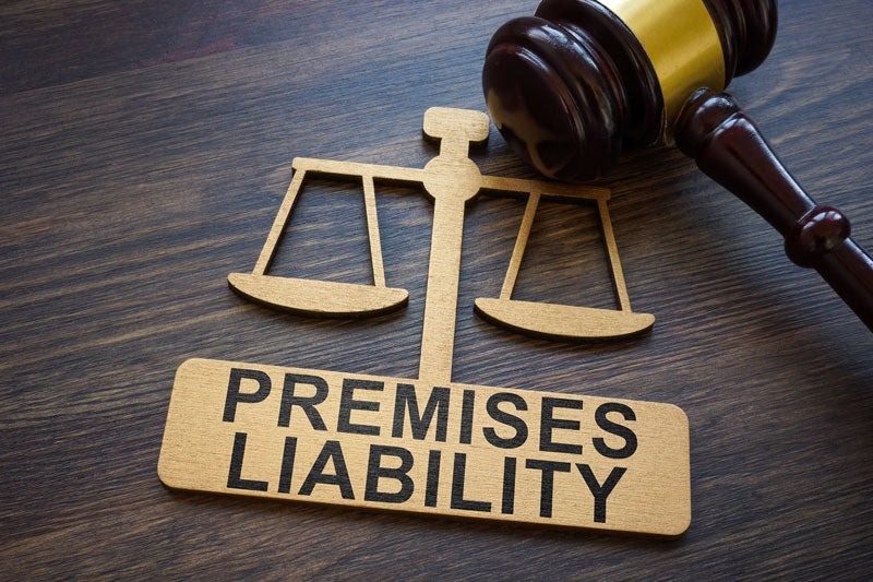 A gavel and scales of justice, with a wooden sign on the bottom that reads PREMISES LIABILITY