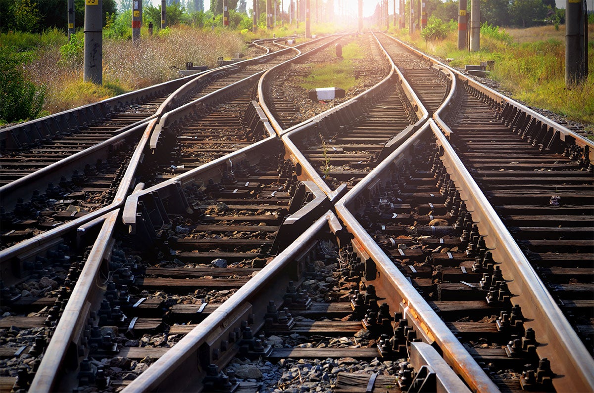 Railway tracks diverge into multiple paths, stretching toward a bright, sunlit horizon.
