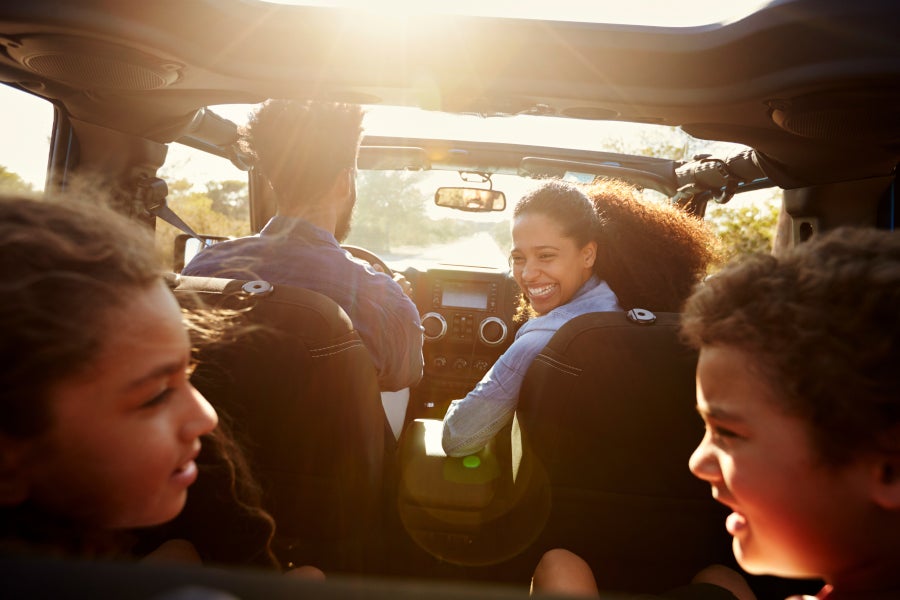 A family of four, including two children, on a sunny road trip inside a convertible car.