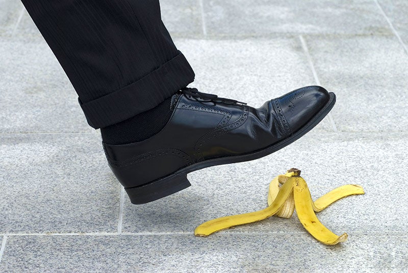 A person's shoe about to step on a banana peel on a tiled sidewalk, indicating potential danger or a mistake.