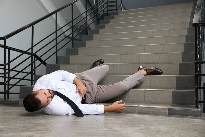 A man in a suit falls down a flight of tiled stairs, appearing injured.