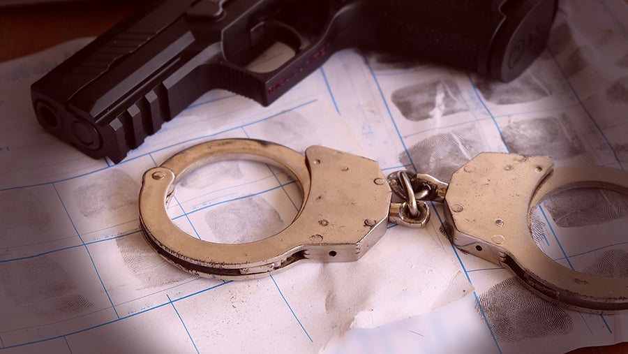 A black gun and silver handcuffs rest on a fingerprint sheet, suggesting crime investigation or arrest.