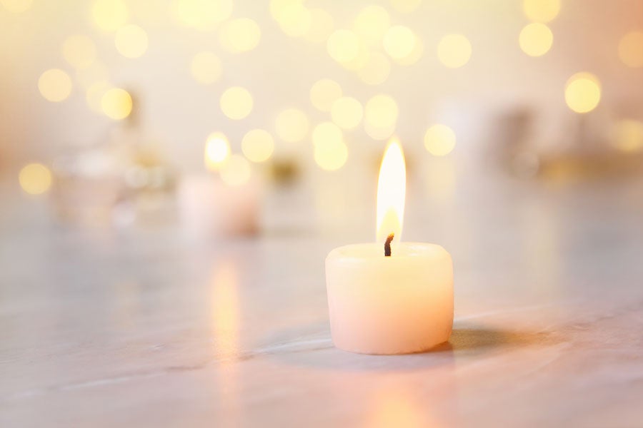 A single, lit candle in the foreground on a marble surface with blurred golden lights in the background.